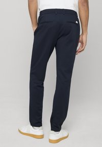 Pantalon bleu marine en tissu doux, avec une coupe droite, des poches arrière et une ceinture avec passants. Porté avec des baskets blanches.