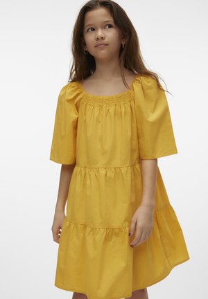 Gul bomulds kjole med firkantet halsudskæring, puffede ærmer og en lagdelt nederdel. Glat tekstur med rynkede detaljer omkring halsen.