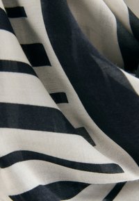 Schwarz-cremefarben gemusteter Seidenstoff mit horizontalen und vertikalen Streifen, der eine glatte Textur und ein fließendes Design zeigt.