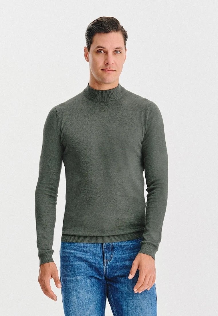 Ciemnozielony sweter z golfem, wykonany z gładkiego materiału, z długimi rękawami i dopasowanym krojem, w połączeniu z niebieskimi dżinsami.