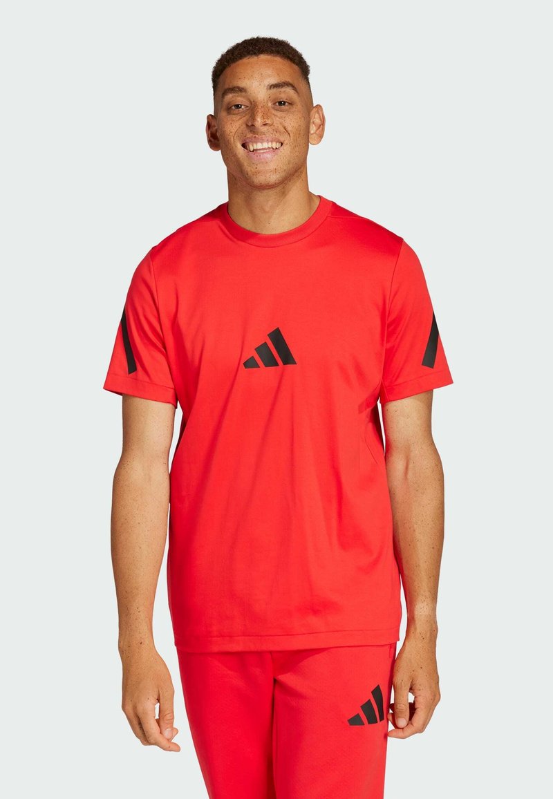 Camiseta deportiva roja con acentos de tres rayas negras en las mangas y un logo negro en el centro. Diseño ligero con cuello redondo.