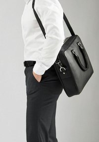 Sort læder skuldertaske med struktureret overflade, to top-håndtag og justerbar rem, præsenteret mod en neutral baggrund.