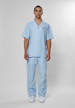Light blue linen short-sleeve shirt with a collar and buttons, paired with matching lightweight trousers. White sneakers complete the outfit.