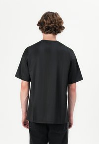 Sort kortærmet T-shirt, lavet af glat stof, har en afslappet pasform og rund halsudskæring. Enkel design uden synlige mønstre.