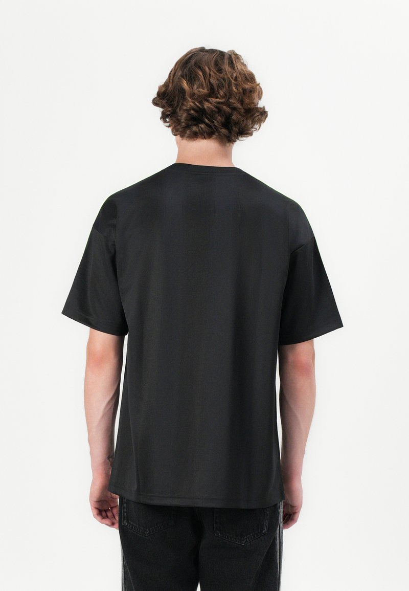 Camiseta negra de manga corta, hecha de una tela suave, presenta un corte holgado y un cuello redondo. Diseño liso sin patrones visibles.