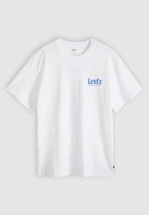 Baltas Levi's trumpomis rankovėmis marškinėlis su mėlynu logotipo tekstu kairėje krūtinės pusėje ir mažu raudonu etiketės kampeliu šone, ant šviesiai pilkos spalvos fono.