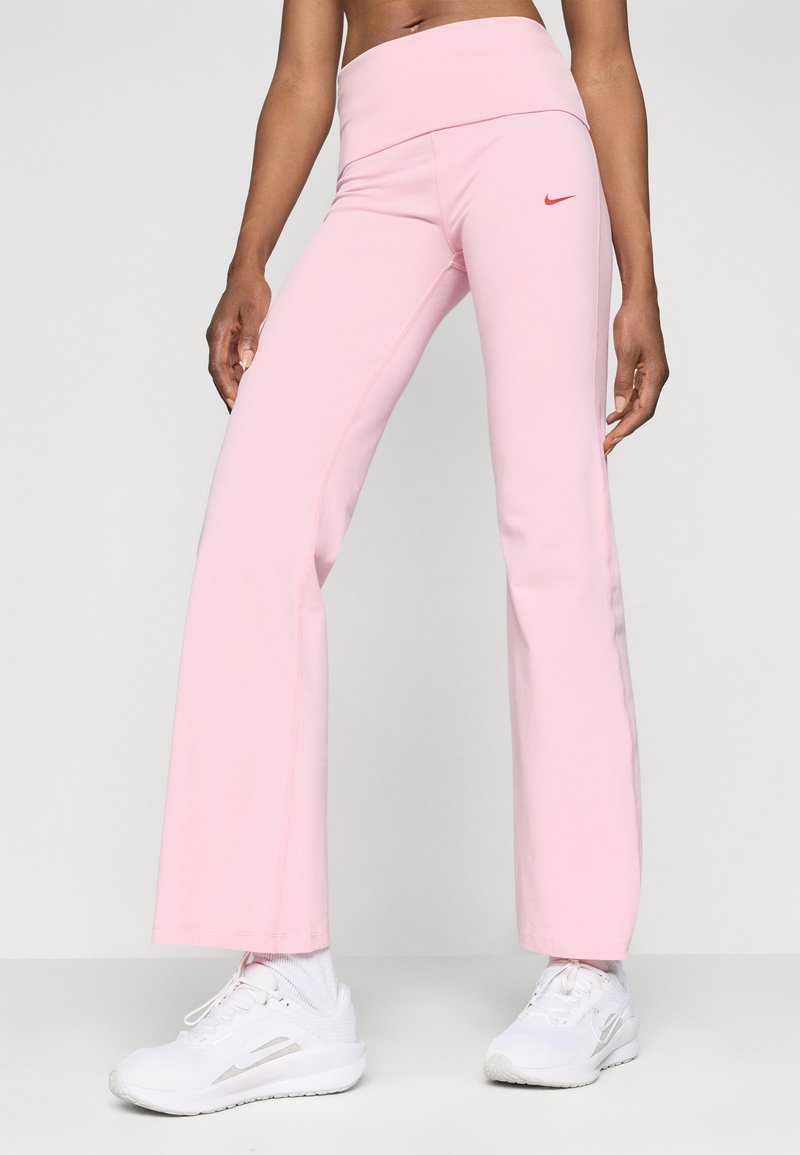 Pantaloni sportivi rosa a campana realizzati in tessuto elasticizzato, con una cintura larga e un piccolo logo rosso sul lato sinistro, abbinati a scarpe bianche.