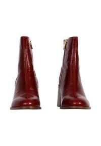 Botas de tobillo de cuero rojo con una textura suave, una forma afilada y un tacón de bloque sturdy. Con cremallera lateral para ponerlas y quitarlas con facilidad.