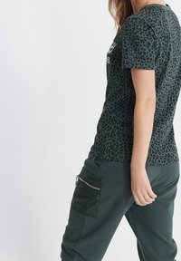 T-shirt w zielony lamparta w kratę, krótki rękaw, w połączeniu z ciemnozielonymi spodniami dresowymi z zamkiem błyskawicznym i miękkim materiałem.