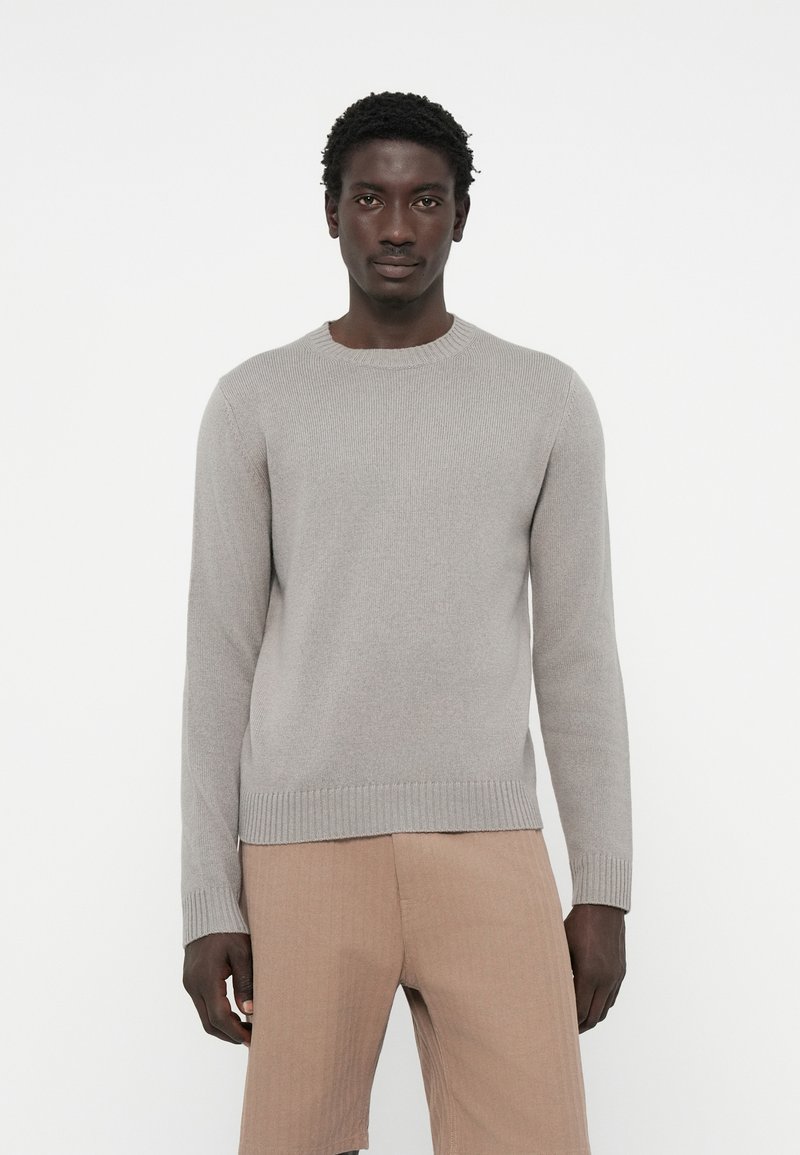 Hellgrauer Strickpullover mit rundem Halsausschnitt und gerippten Manschetten, leicht taillierte Passform, kombiniert mit beigen Shorts, glatte Textur, schlichte Optik.