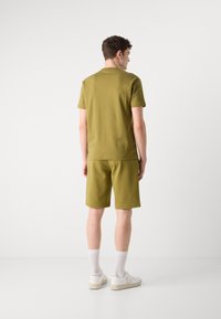 Set format din bumbac de culoare verde măsliniu, compus dintr-o bluză cu mânecă scurtă și pantaloni scurți, croială lejeră, cu un brâu elastic, asortat cu adidași albi și șosete tip crew.