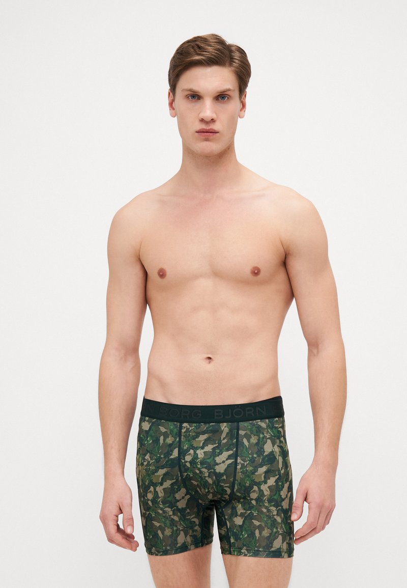 Boxer-briefs à motif camouflage dans des nuances de vert, fabriqués en tissu extensible. Dotés d'une ceinture élastique noire avec l'inscription de la marque.