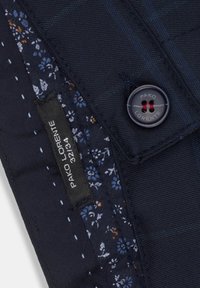 Granatowy materiał z delikatnym wzorem w kratkę, z kwiatową podszewką. Widoczny jest ciemny guzik z czerwonymi akcentami, oznaczony PAKO LORENTE.