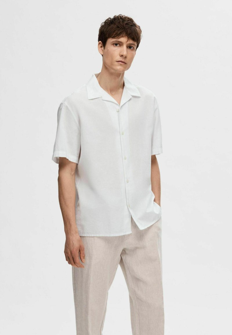 Camicia bianca a maniche corte con bottoni in tessuto leggero e strutturato; vestibilità rilassata con colletto a punta e dettagli dei bottoni discreti.