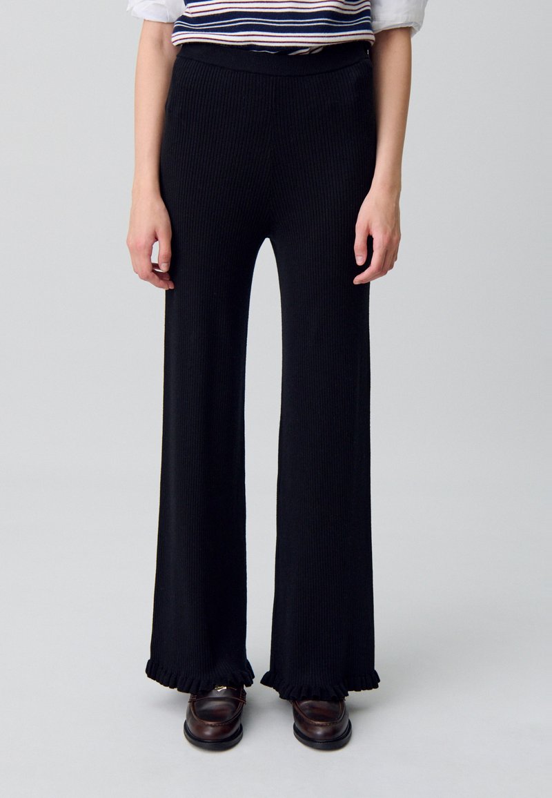 Pantalones de pierna ancha de rayas negras con un acabado texturizado y dobladillo con volantes. Presentan una cinturilla suave y bolsillos laterales sutiles.