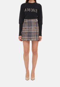 Pull marin avec "AMORE" en lettres claires et une jupe à carreaux présentant des couleurs marron, noir et rouge, avec deux boutons et un détail en frange.