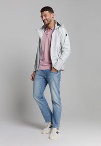 Witte waterdichte jas met capuchon, lichtroze polo shirt, blauwe spijkerbroek en witte sneakers met marineblauwe accenten. Casuale pasvorm, modern ontwerp.