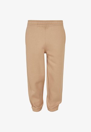 Małe dziecko stoi w beżowym hoodie i pasujących dresach, w białych trampkach Adidas z czarnymi paskami, patrząc lekko w górę.