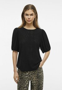 Svart blus med puffärmar, med hålmönster och subtila mönster, i kombination med leopardmönstrade byxor.