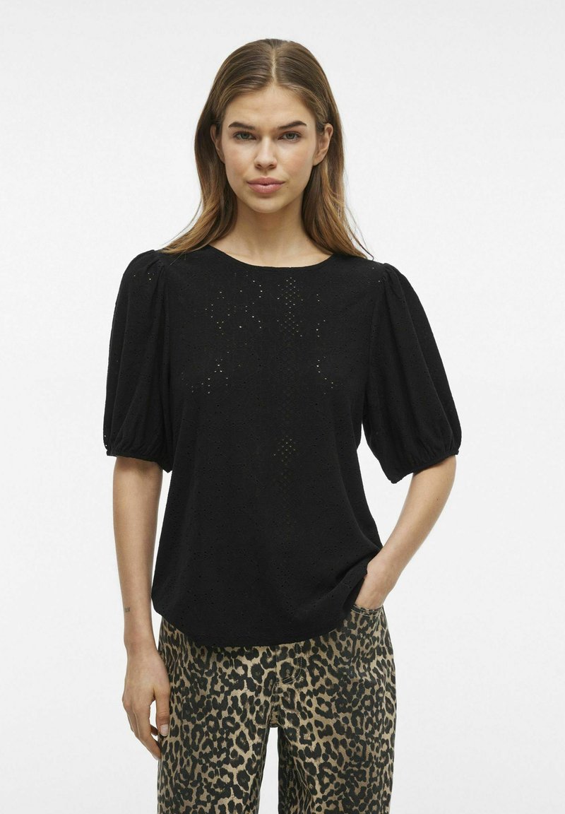 Svart blus med puffärmar, med hålmönster och subtila mönster, i kombination med leopardmönstrade byxor.