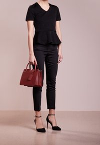 Musta peplum-toppi teksturoitua kangasta, yhdistettynä mustiin tiukkoihin housuihin ja mustiin korkokenkiin. Pitelee pientä viininpunaisesta nahasta valmistettua käsilaukkua.