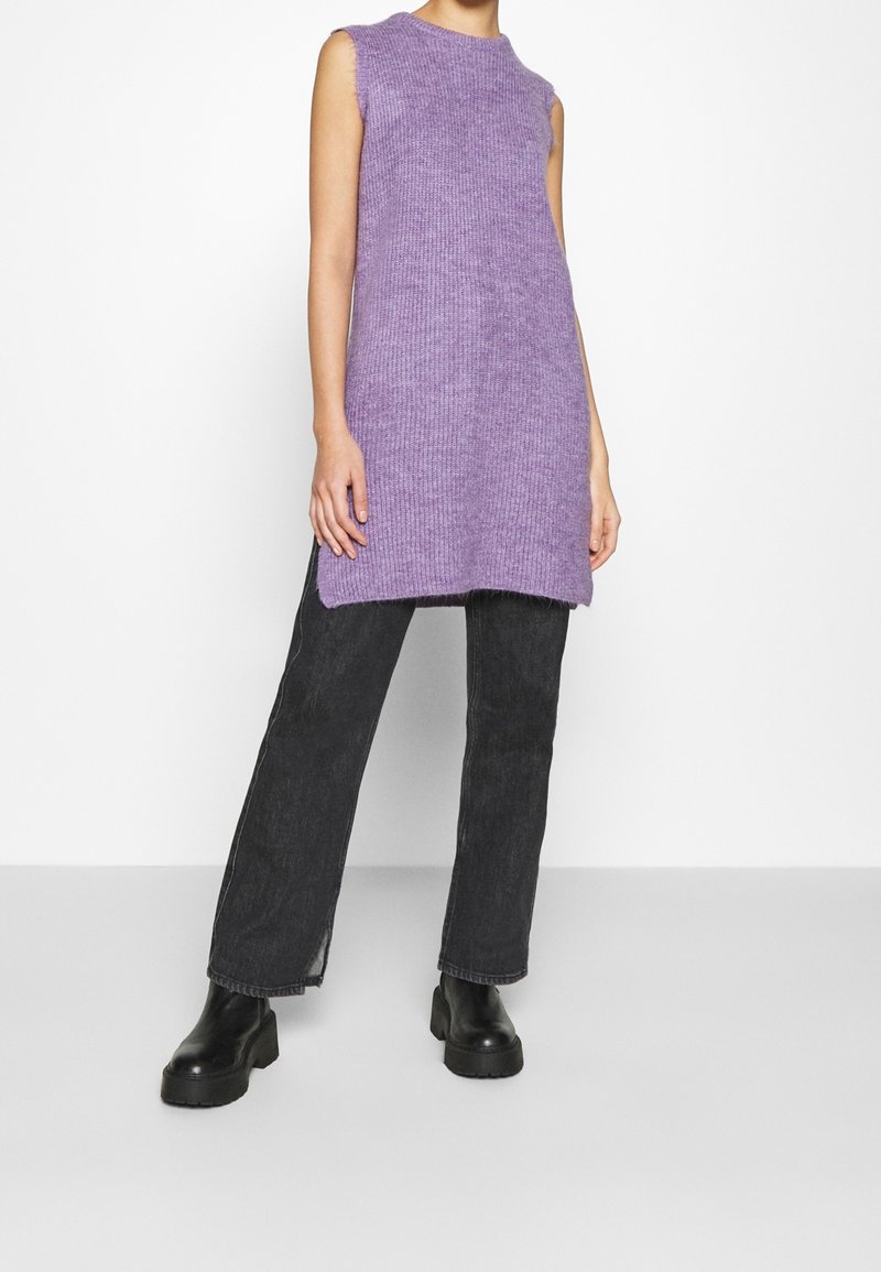 Lila gestricktes ärmelloses Kleid mit geradem Schnitt, kombiniert mit hochtaillierten schwarzen Jeans und klobigen schwarzen Stiefeletten.
