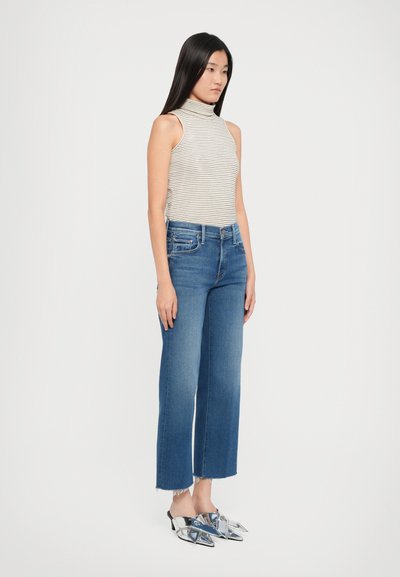 Top senza maniche a collo alto a righe, jeans a gamba larga blu con orli sfrangiati e mule argentate lucide con punta a punta. Design semplice e moderno.