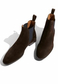 Botines de ante marrón con paneles laterales de elasticidad, puntera lisa y forro interior en un tono marrón claro en contraste. Tacón plano con un diseño minimalista.