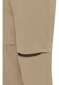 Pantalon beige convertible avec fermeture éclair au niveau du genou, permettant de retirer la partie inférieure de la jambe.