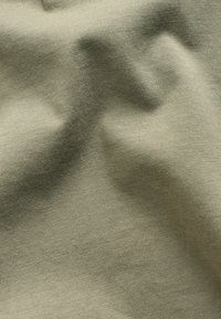Helles olivgrünes Gewebe mit einer glatten, leicht strukturierten Oberfläche und subtiler Dehnbarkeit, das ein detailreiches Strickmuster aufweist.