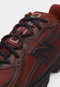 Gros plan sur une chaussure de sport rouge et noire avec des lacets noirs et un grand logo stylisé "N" sur le côté.