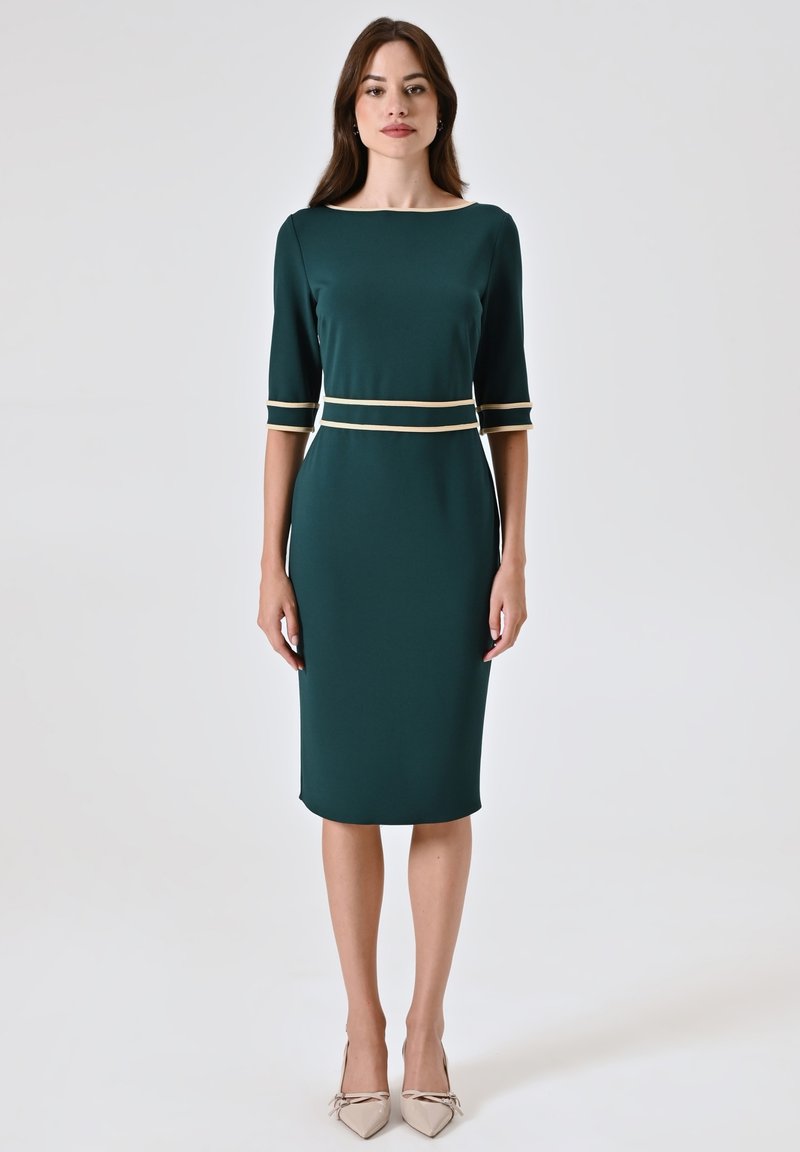Abito aderente verde scuro con maniche a tre quarti, caratterizzato da accenti crema in vita e sulle maniche. Tessuto liscio con orlo a lunghezza ginocchio.