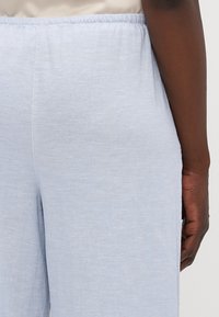 Light blue, relaxed-fit trousers with an elastic waistband, made from a soft, textured fabric. Features a smooth seam along the side.