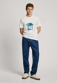 Balta medvilninė marškinėlė su mėlynu grafiniu dizainu ir "Pepe Jeans" tekstu. Derinama su mėlynomis džinsinėmis kelnėmis ir baltomis sportinėmis bateliais. Atsitiktinis siluetas.