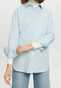 Ljust blå, långärmad skjorta i bomull. Har en knäppning framtill, oversized manschetter och en avslappnad passform. Kombinerad med en vit polotröja under.