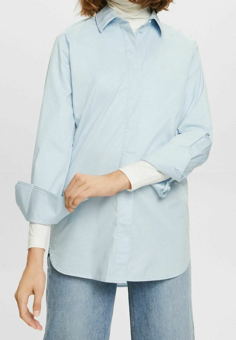 Ljust blå, långärmad skjorta i bomull. Har en knäppning framtill, oversized manschetter och en avslappnad passform. Kombinerad med en vit polotröja under.