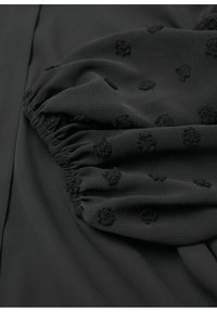 Tissu noir avec des pois texturés en relief et un détail élastique froncé sur un fond textile noir lisse.