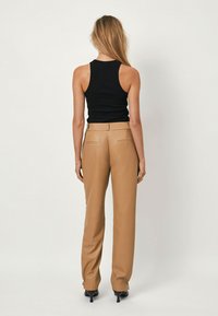 Beige op maat gemaakte broeken met een gladde textuur en achterzakken, gecombineerd met een aansluitend zwart mouwloos topje. Minimalistisch ontwerp en strakke lijnen.