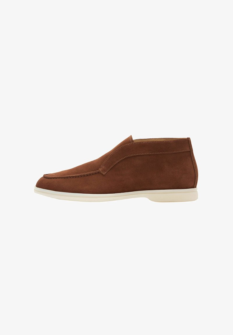 Chaussure slip-on en suède marron avec une finition lisse, un bout légèrement pointu et une semelle en caoutchouc blanc contrastant. Détails de couture minimalistes.