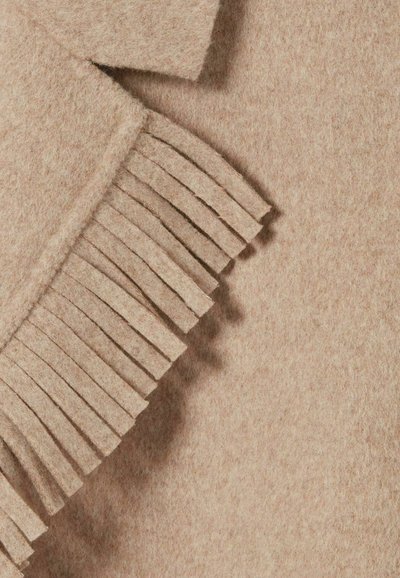 Gros plan sur un tissu en laine beige avec un détail de bord frangé sur un vêtement plié.