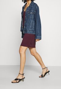 Džínová bunda v středně modrém odstínu s knoflíkovým zapínáním a dvěma náprsními kapsami, kombinovaná s přil éhavými vínovými šaty a černými páskovými podpatky.