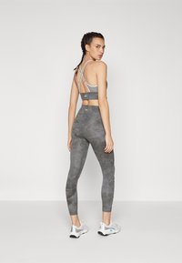 Sporting set features a gray cropped top with crisscross straps and matching high-waisted leggings with a subtle pattern. Silver athletic shoes complete the look.