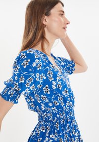 Vestido floral azul con patrones en blanco y negro. Mangas cortas abullonadas y cintura fruncida. Tejido ligero con una silueta fluida.