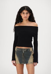 Svart ribbestrikket crop top uten skuldre kombinert med et mini-skjørt i lappeteppe av denim, med sidelapper og glidelås foran.
