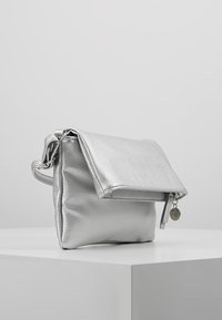 Silver faux leather bag with a fold-over flap, smooth texture, and side zipper. Features a decorative charm on the zipper pull.