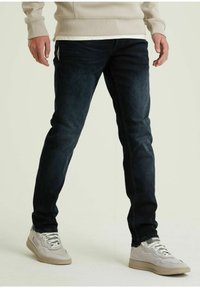 Jeans in denim blu scuro con una vestibilità slim, caratterizzati da un classico design a cinque tasche e una finitura pulita, abbinati a sneakers grigio chiaro.