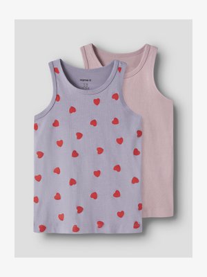 Dos camisetas sin mangas para niño pequeño, una lila con corazones rojos dispersos, otra lisa de color rosa claro, colocadas planas sobre un fondo claro.