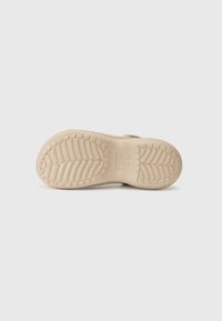 Semelle d'une chaussure Crocs beige montrant un motif de la bande de roulement avec des crêtes horizontales et inclinées sur un fond gris clair.