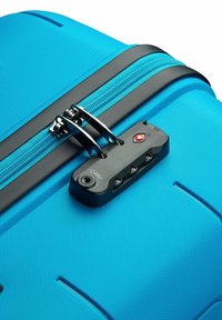 Maleta rígida de color azul brillante con superficie texturizada, cremallera negra, dos tiradores negros y cierre aprobado por la TSA con acento rojo.