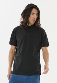 Sort polo shirt fremstillet af bomuld med klassisk krave, placket med tre knapper og korte ærmer. Har et diskret logo på venstre bryst.